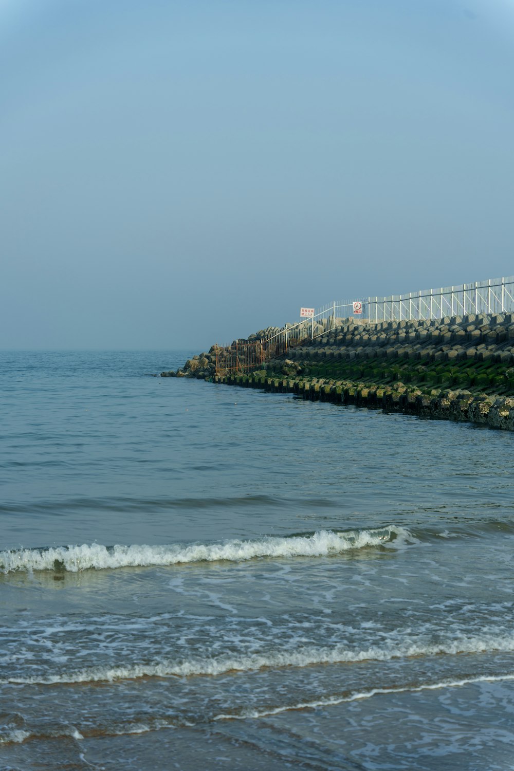 a body of water next to a beach with a white fence