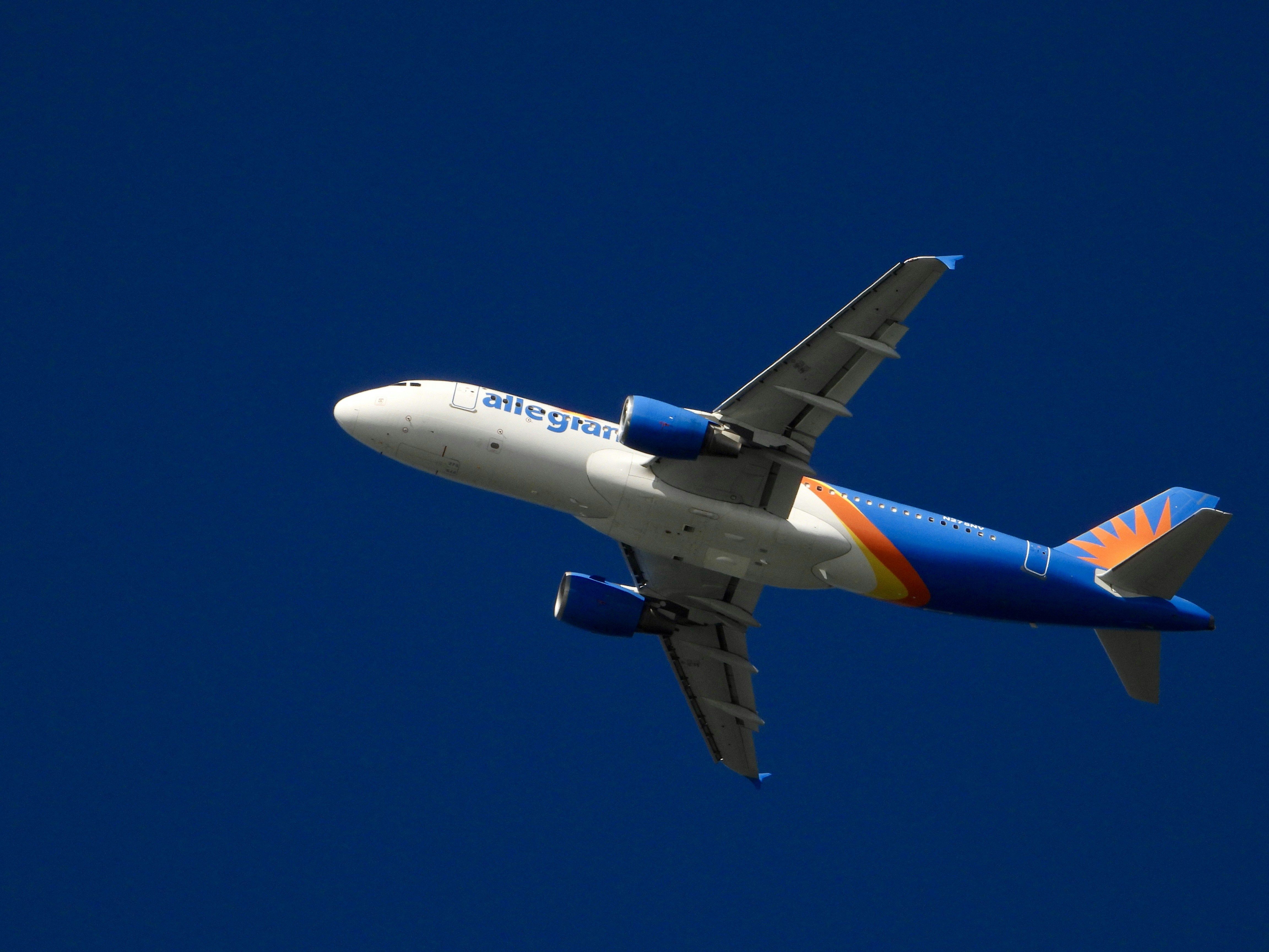 a blue and white airplane flying in a blue sky, There goes an Allegiant airplane flying by photographer Anita Denunzio.
