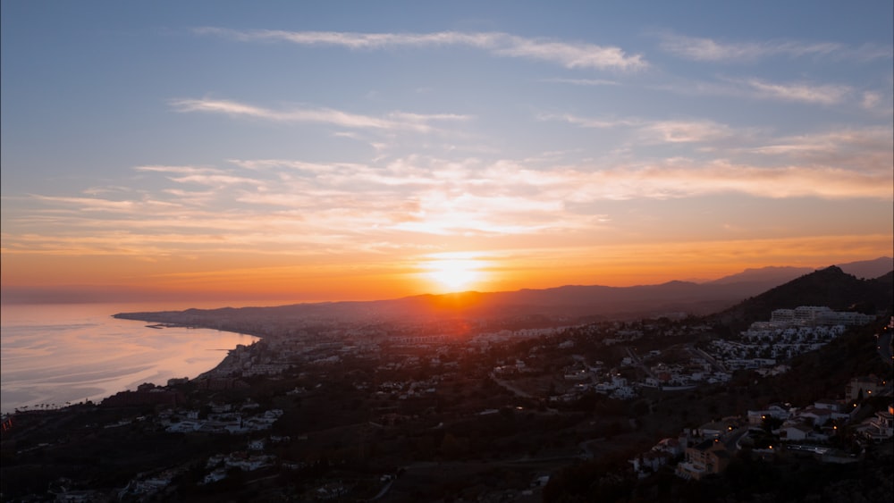 the sun is setting over a city and the ocean