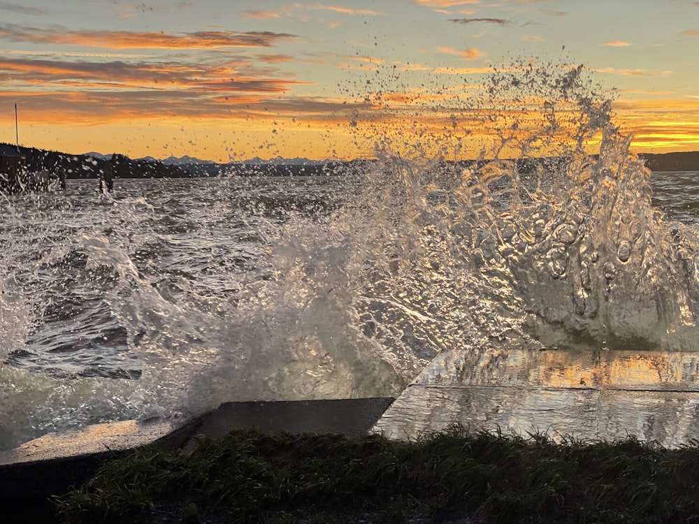 a large wave crashing into the shore at sunset