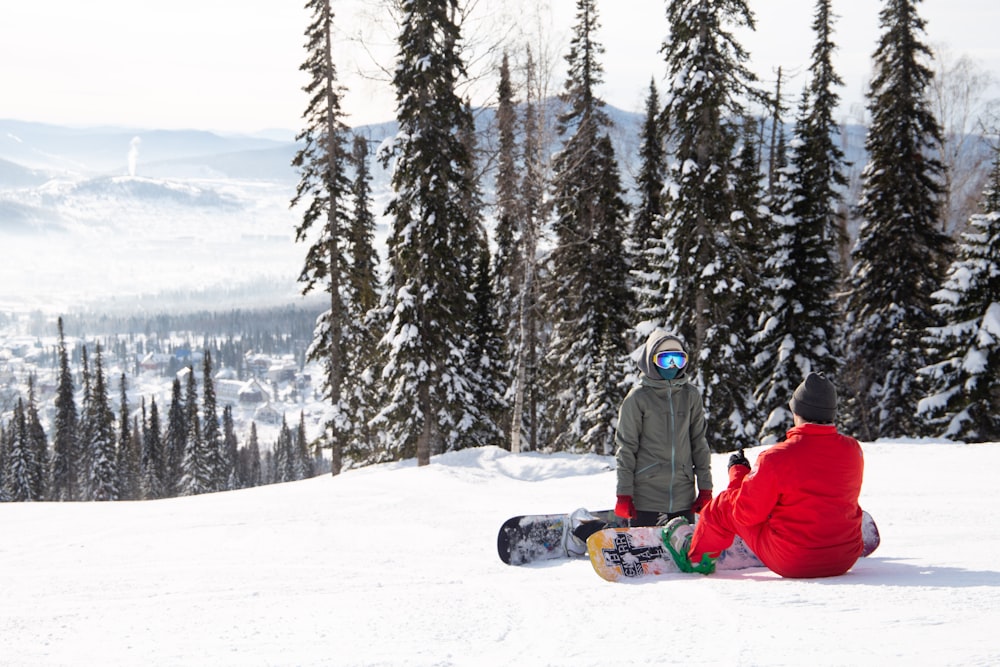 two people sitting in the snow with snowboards