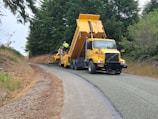 a yellow dump truck driving down a curvy road