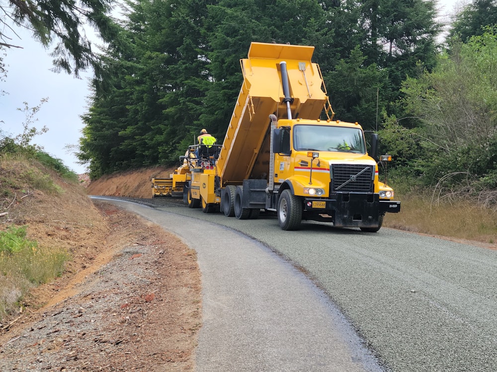 a yellow dump truck driving down a curvy road