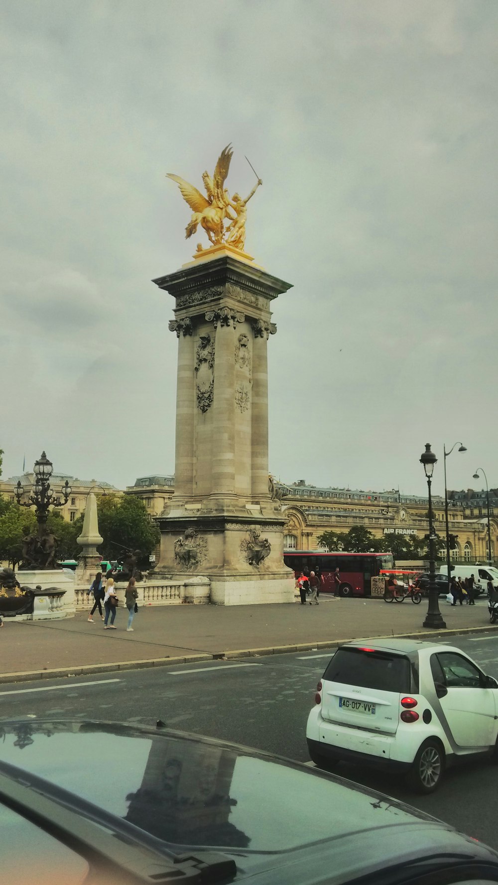 a white car driving down a street next to a golden statue