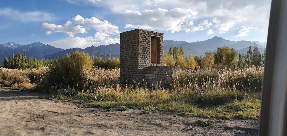 une petite structure en brique dans un champ avec des montagnes en arrière-plan