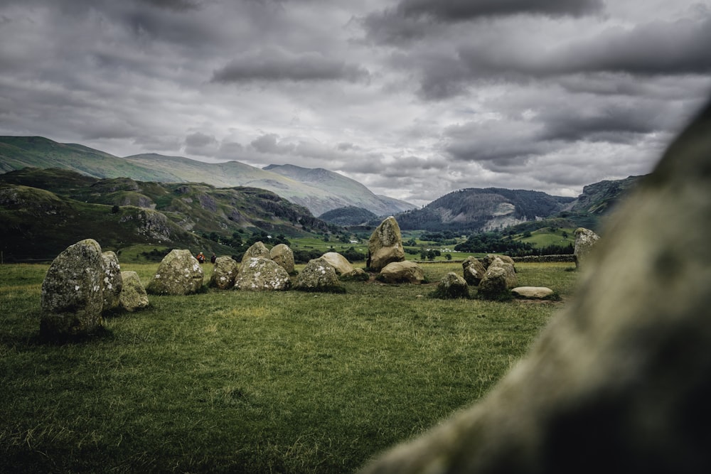 a grassy field with rocks in the foreground and mountains in the background