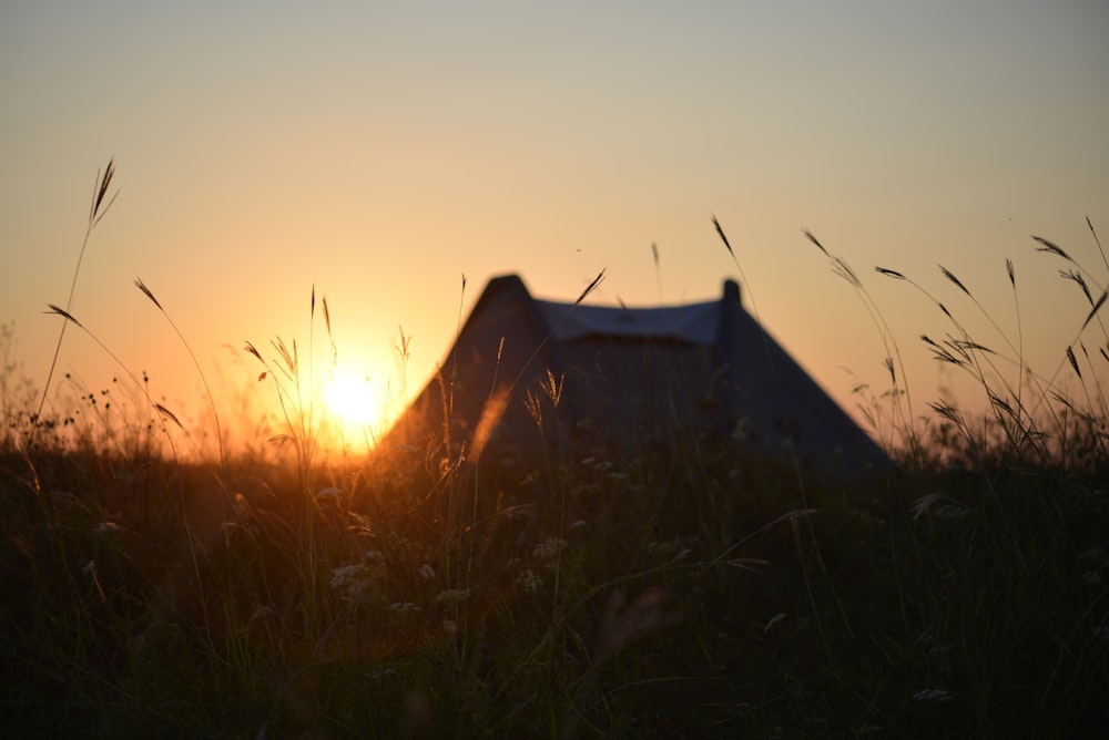 the sun is setting behind a tent in a field