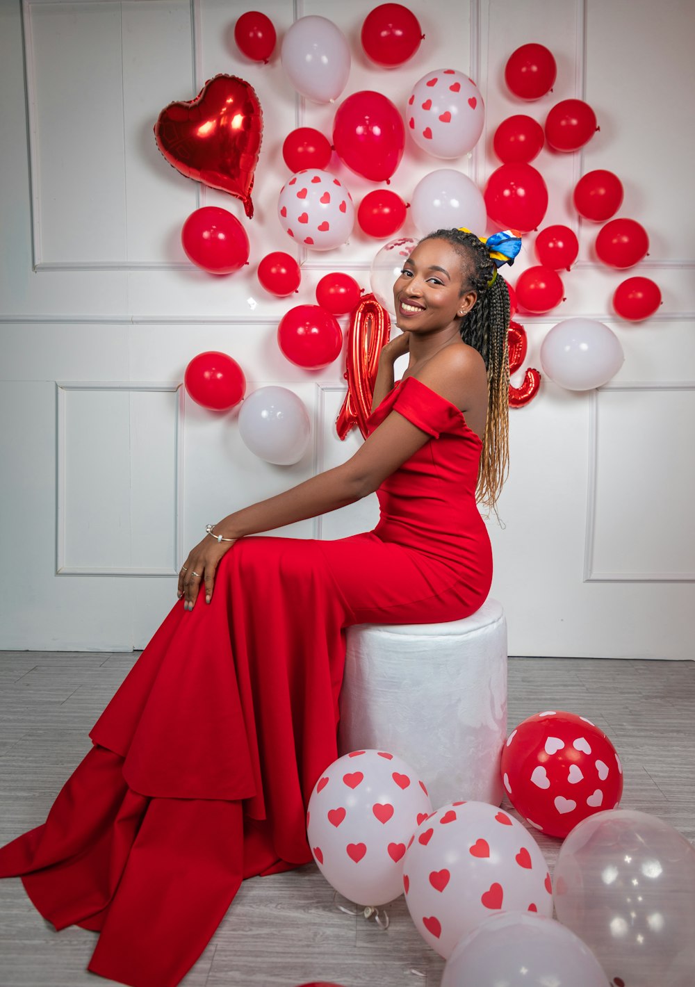 a woman in a red dress sitting on a stool surrounded by balloons