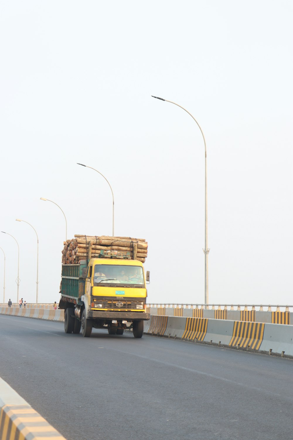 a yellow truck driving down a road next to a bridge
