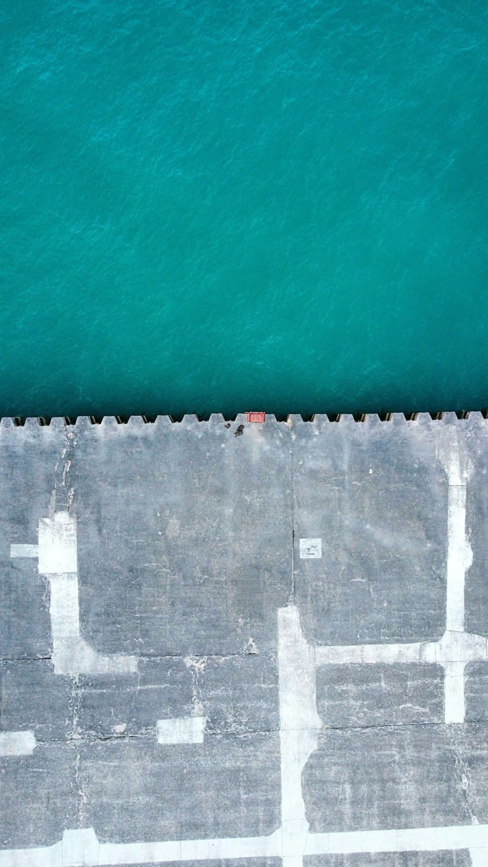 an aerial view of a concrete walkway next to a body of water