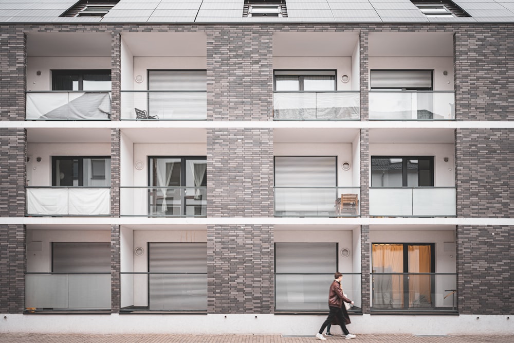 une personne qui passe devant un grand bâtiment en brique