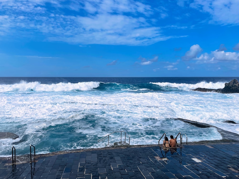 a couple of people sitting on a bench near the ocean