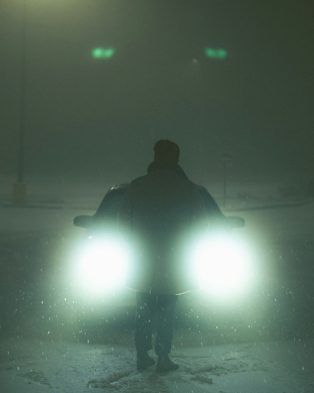 a man standing in the snow with two headlights