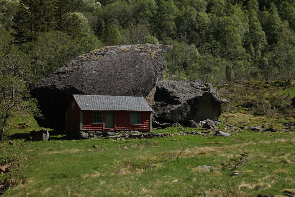 a small red cabin sitting next to a large rock