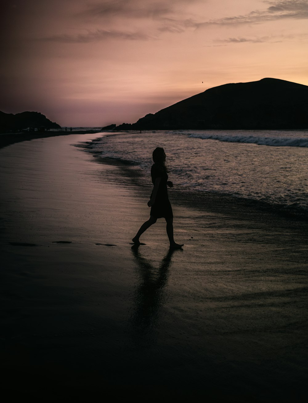 a person walking on a beach at sunset