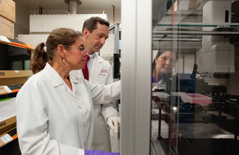 a man and a woman in lab coats looking at something in a cabinet