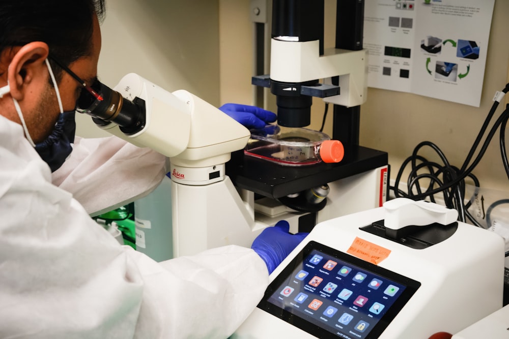 a man in white lab coat looking through a microscope