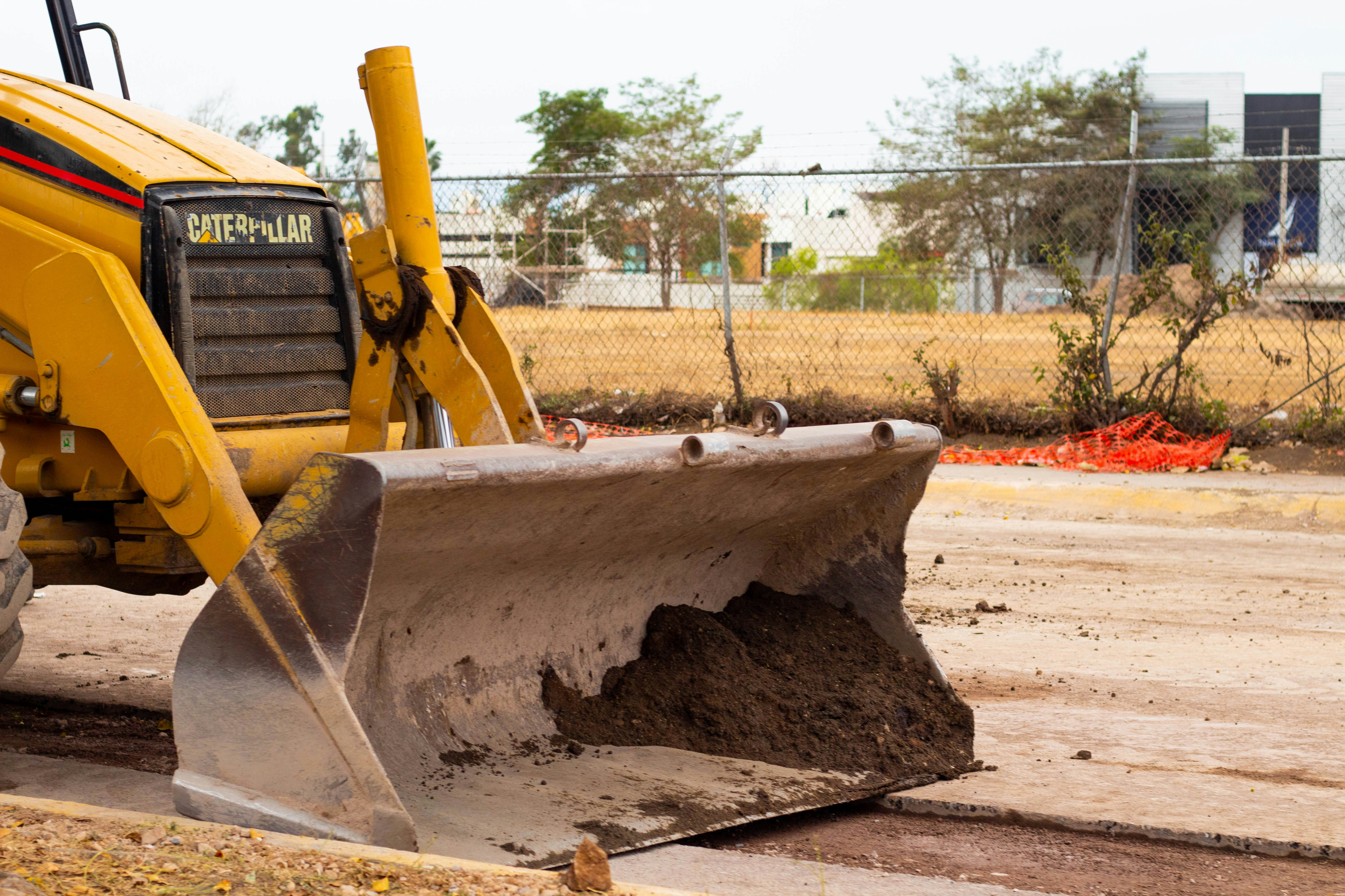 Yellow TLB backhoe loader on construction site, front bucket raised, versatile utility machinery