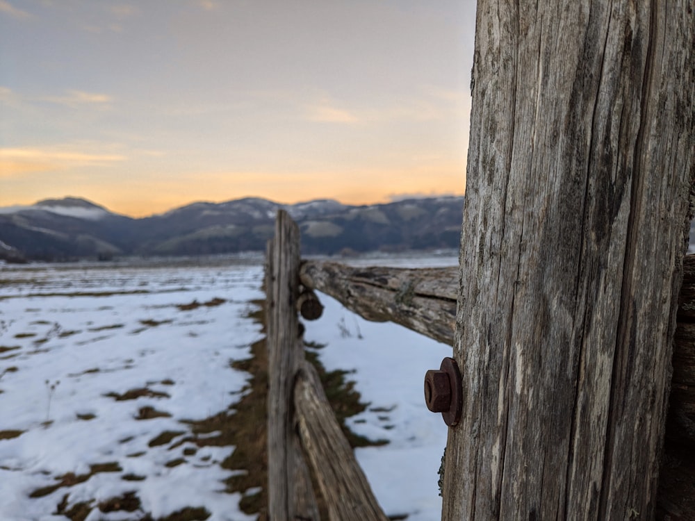a wooden fence in a snowy field with mountains in the background