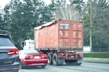 a red truck driving down a street next to a forest