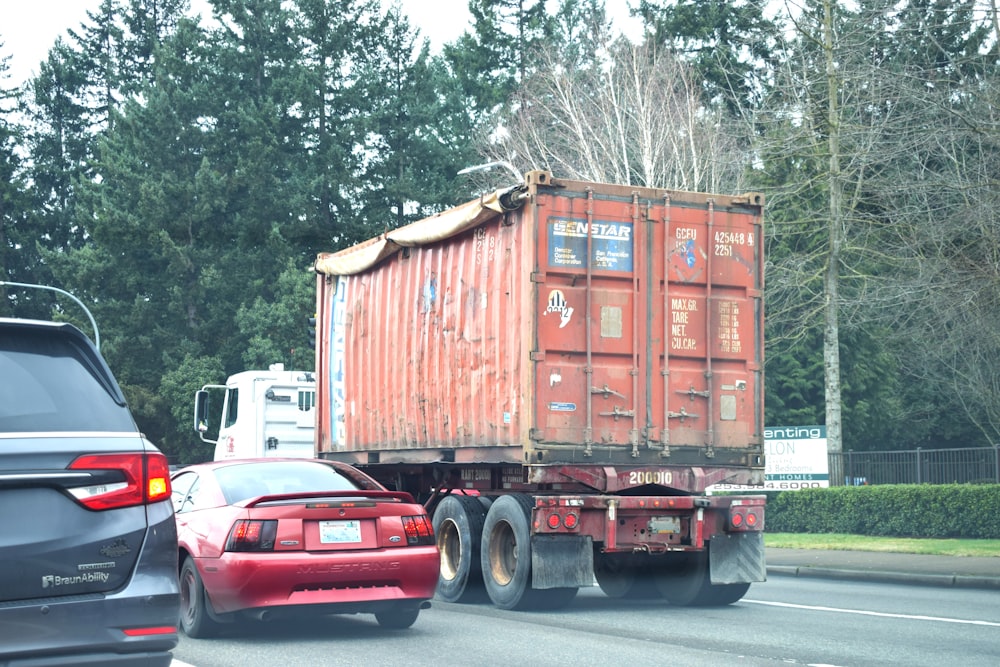 a red truck driving down a street next to a forest