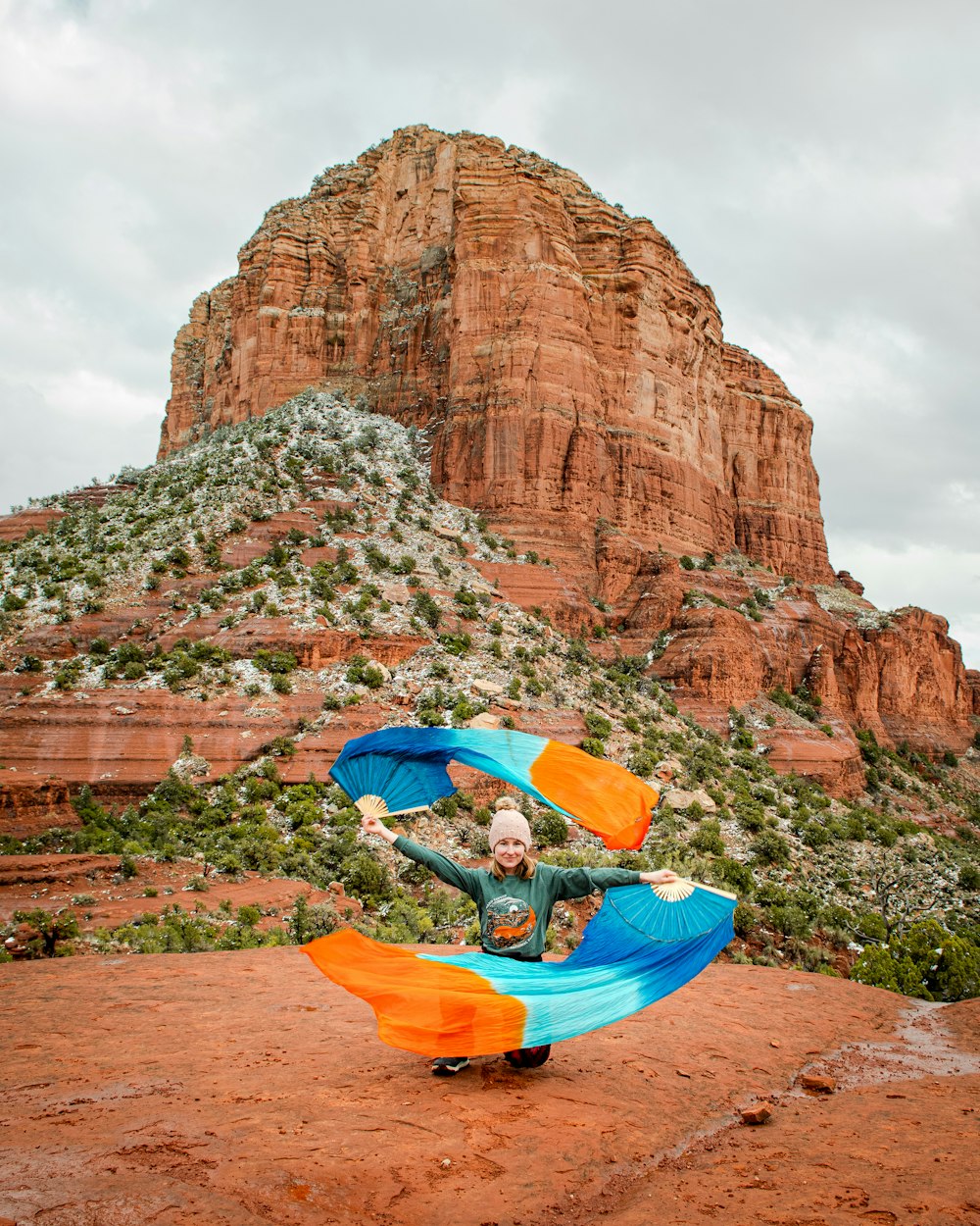 a man holding a blue and orange kite in front of a mountain