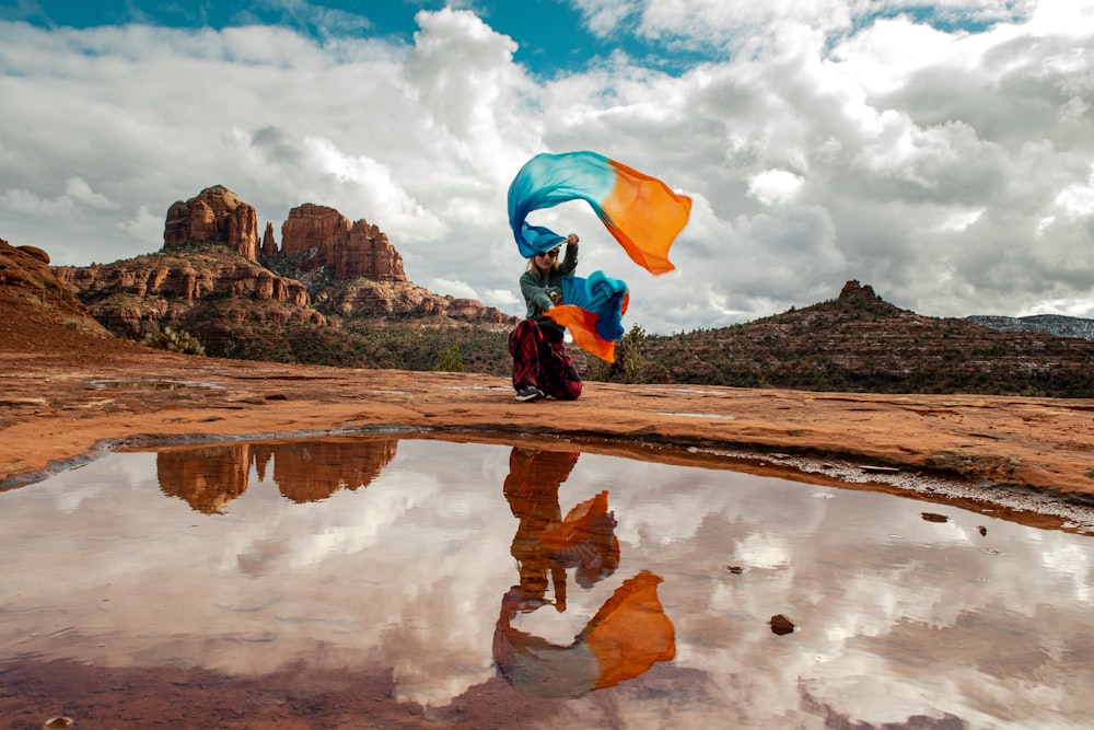 a woman holding a blue and orange umbrella next to a body of water