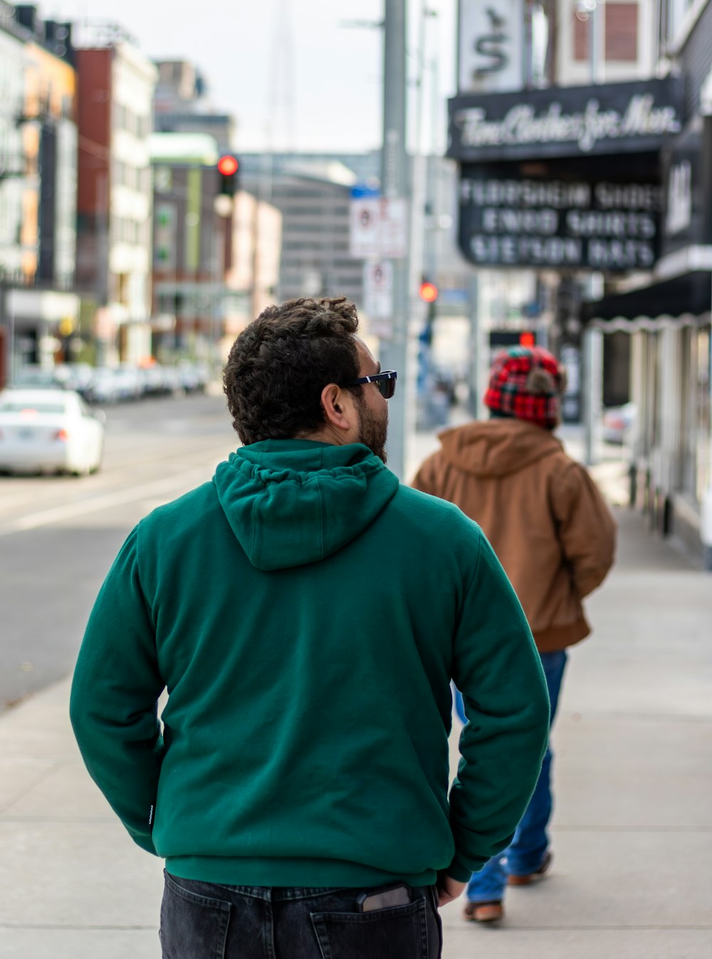 a man in a green hoodie walking down a sidewalk