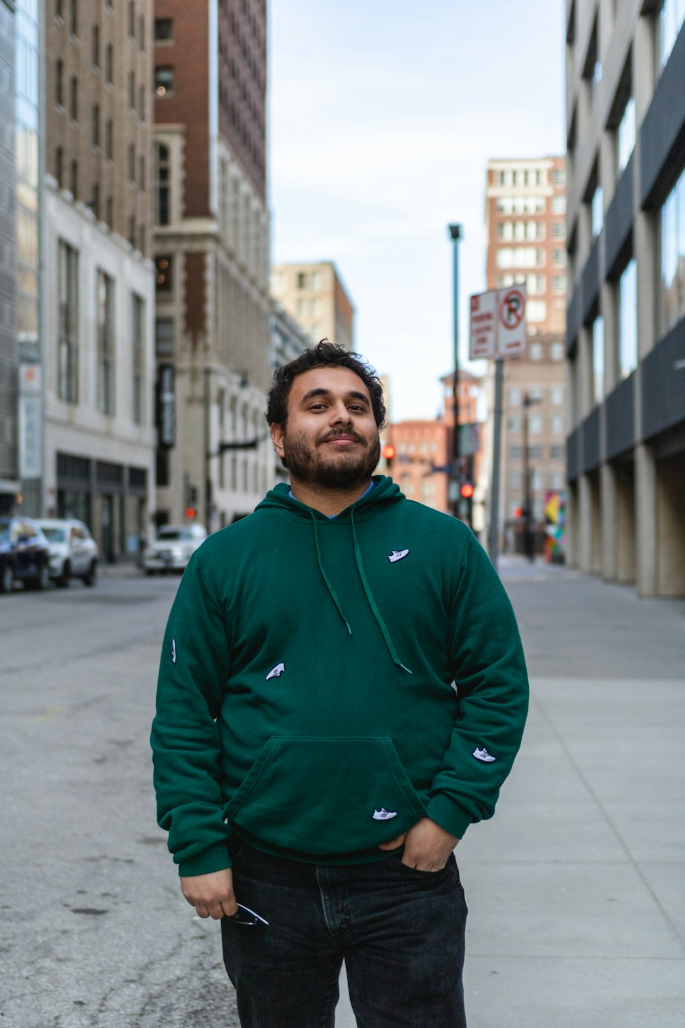 a man in a green hoodie standing on a sidewalk