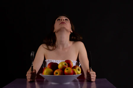 a woman sitting at a table with a bowl of apples