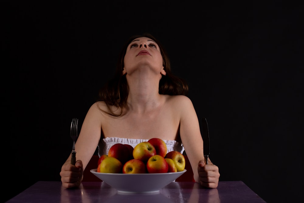 una mujer sentada en una mesa con un cuenco de manzanas