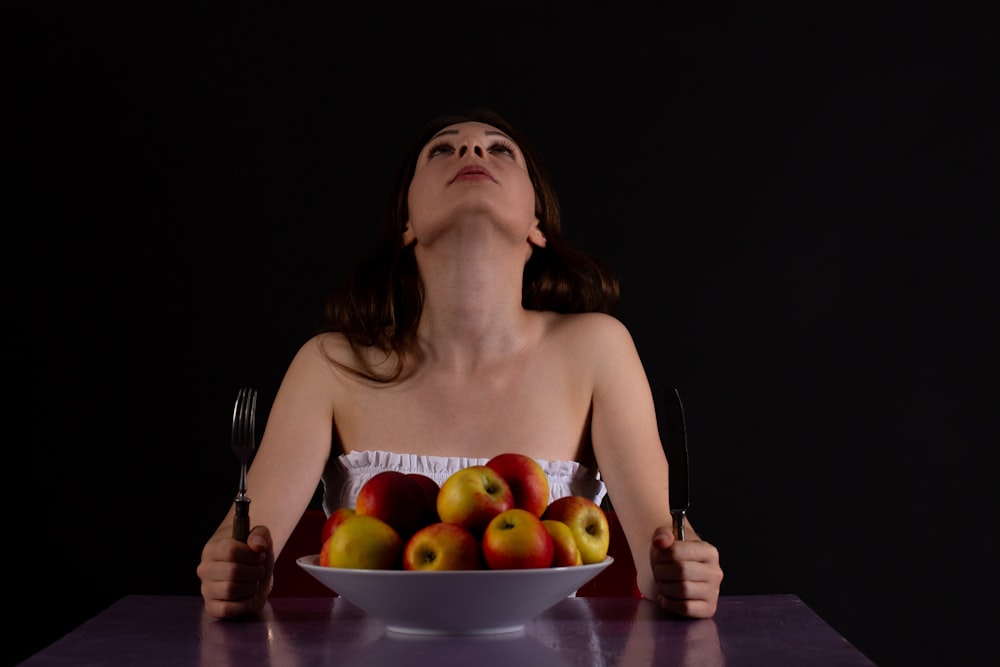 a woman sitting at a table with a bowl of apples