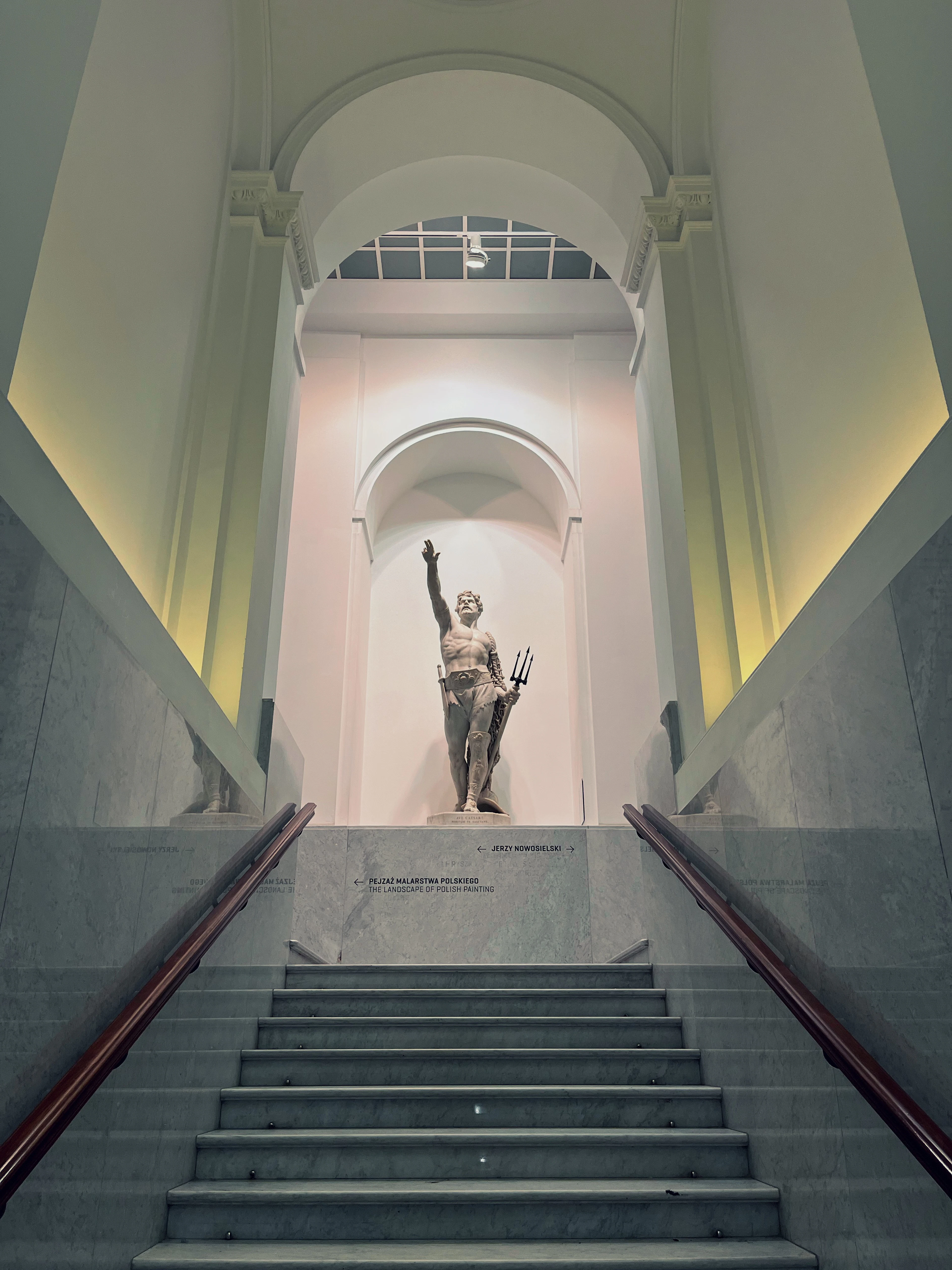 A marble staircase rises toward a statue holding a trident, dramatically lit inside a museum hall.