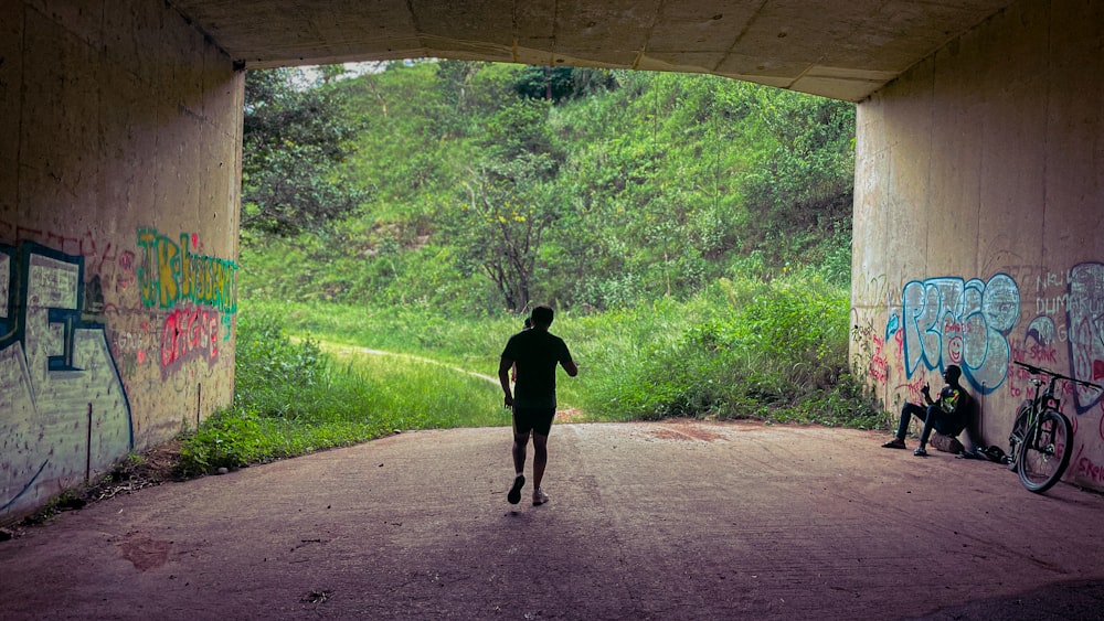 a man walking through a tunnel covered in graffiti