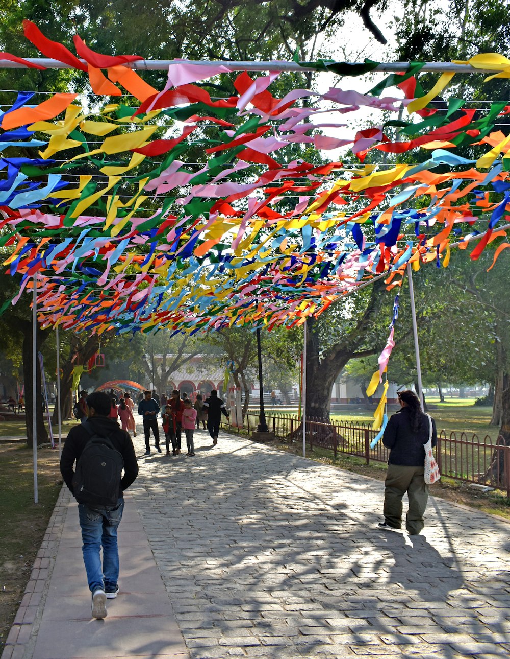 a group of people walking down a sidewalk under a canopy of colorful streamers