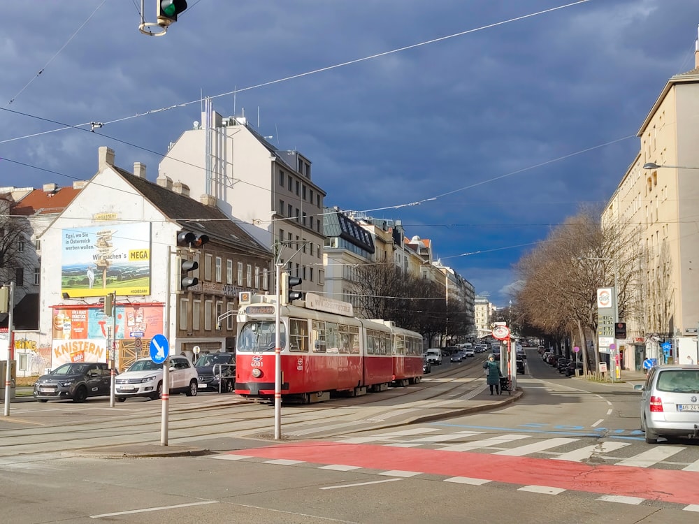 a red train traveling down a street next to tall buildings