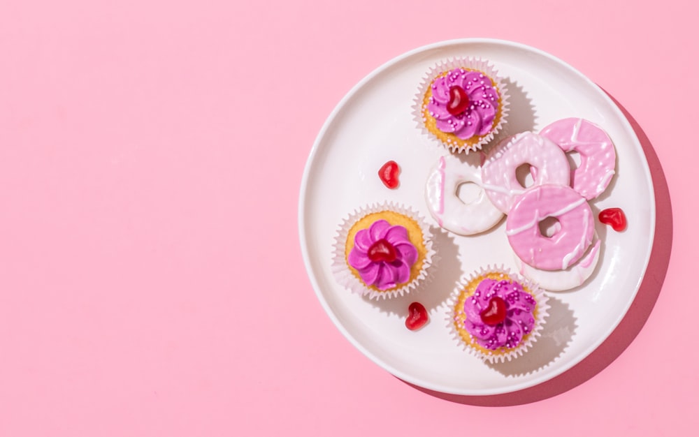 a white plate topped with cupcakes covered in pink frosting