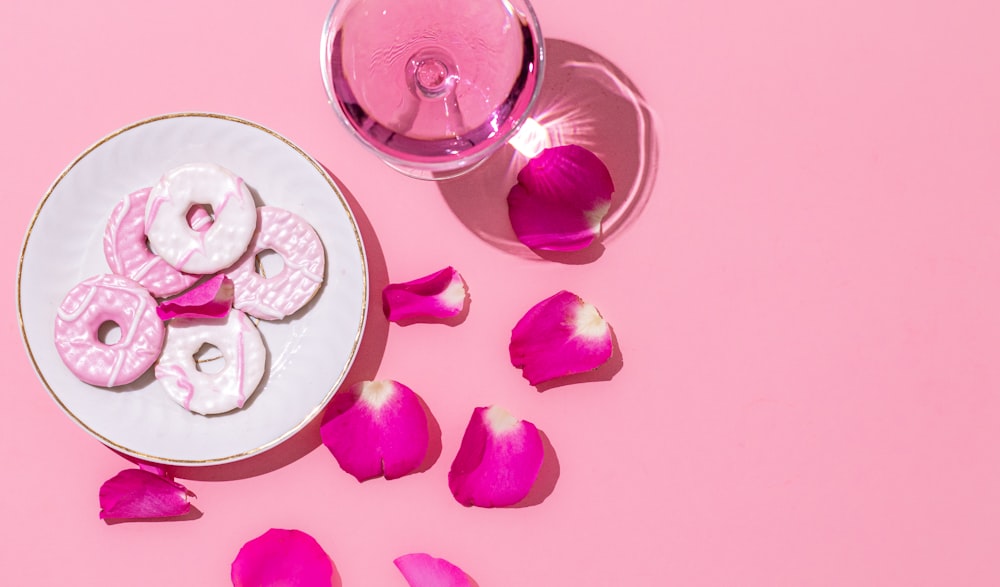 a white plate topped with pink donuts next to a glass of wine