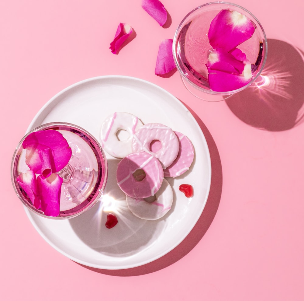 two glasses of water with pink petals on a plate