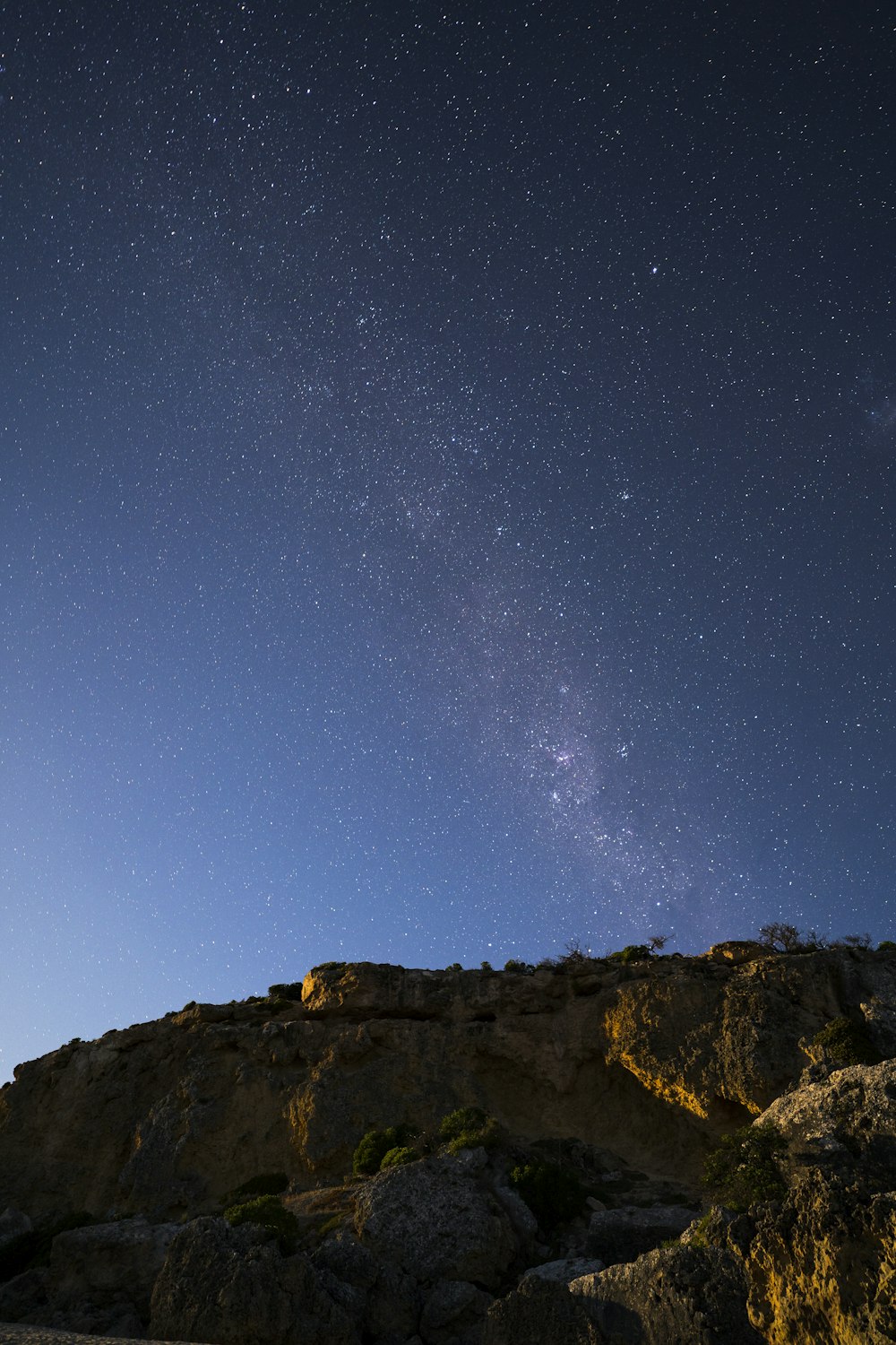 the night sky with stars above a rocky hill