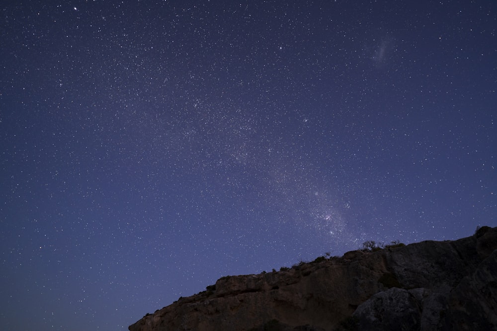 the night sky with stars above a rocky outcropping