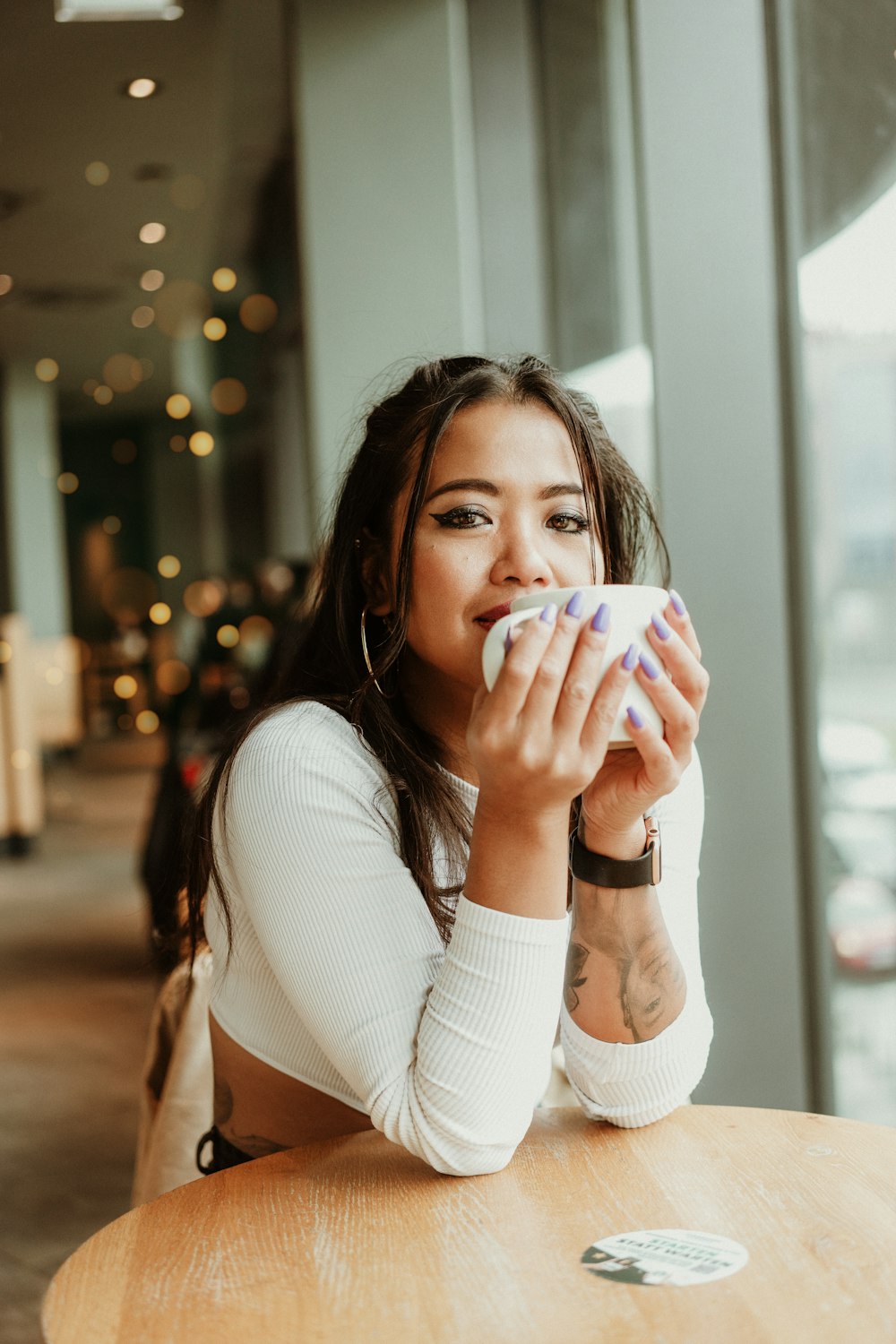 a woman sitting at a table drinking from a cup