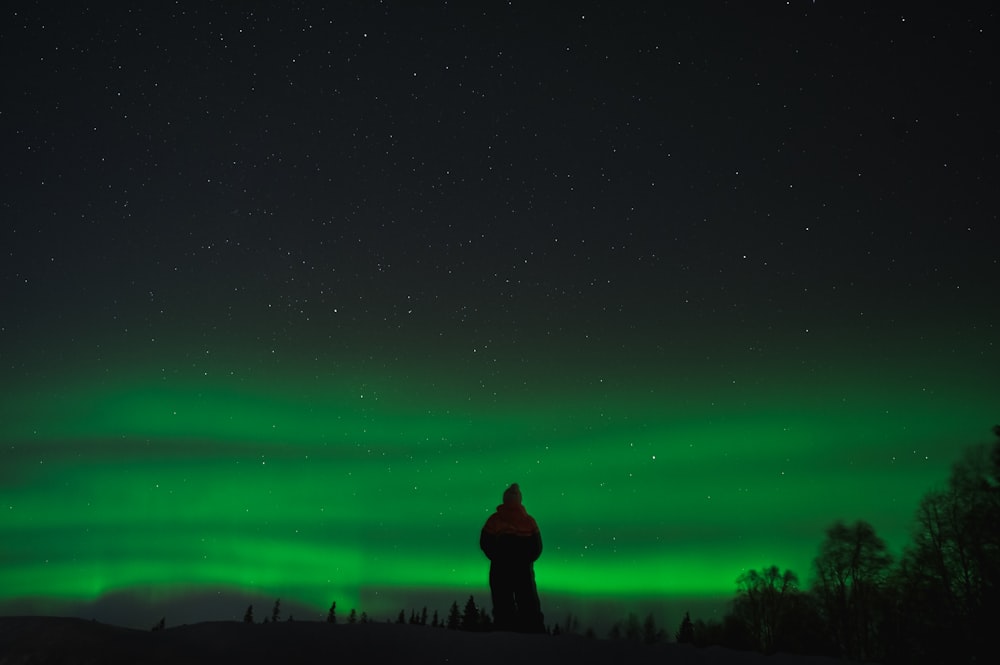 a person standing on top of a snow covered hill under a green sky