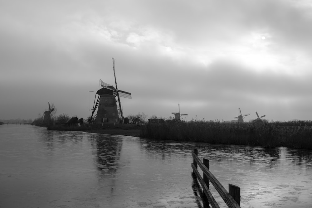 a black and white photo of a river and windmills