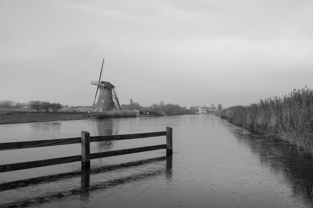 une photo en noir et blanc d’une rivière avec un moulin à vent en arrière-plan
