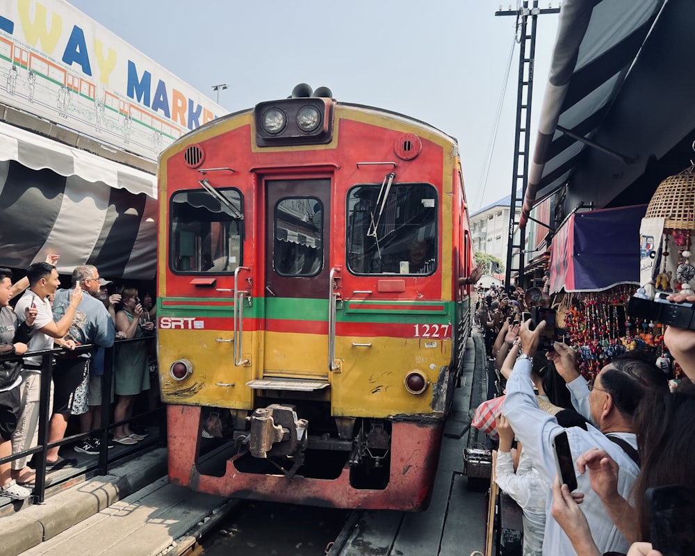 a red and yellow train traveling past a crowd of people