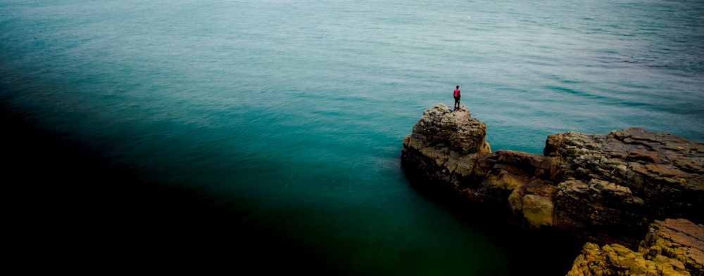 a person standing on a rock in the middle of a body of water