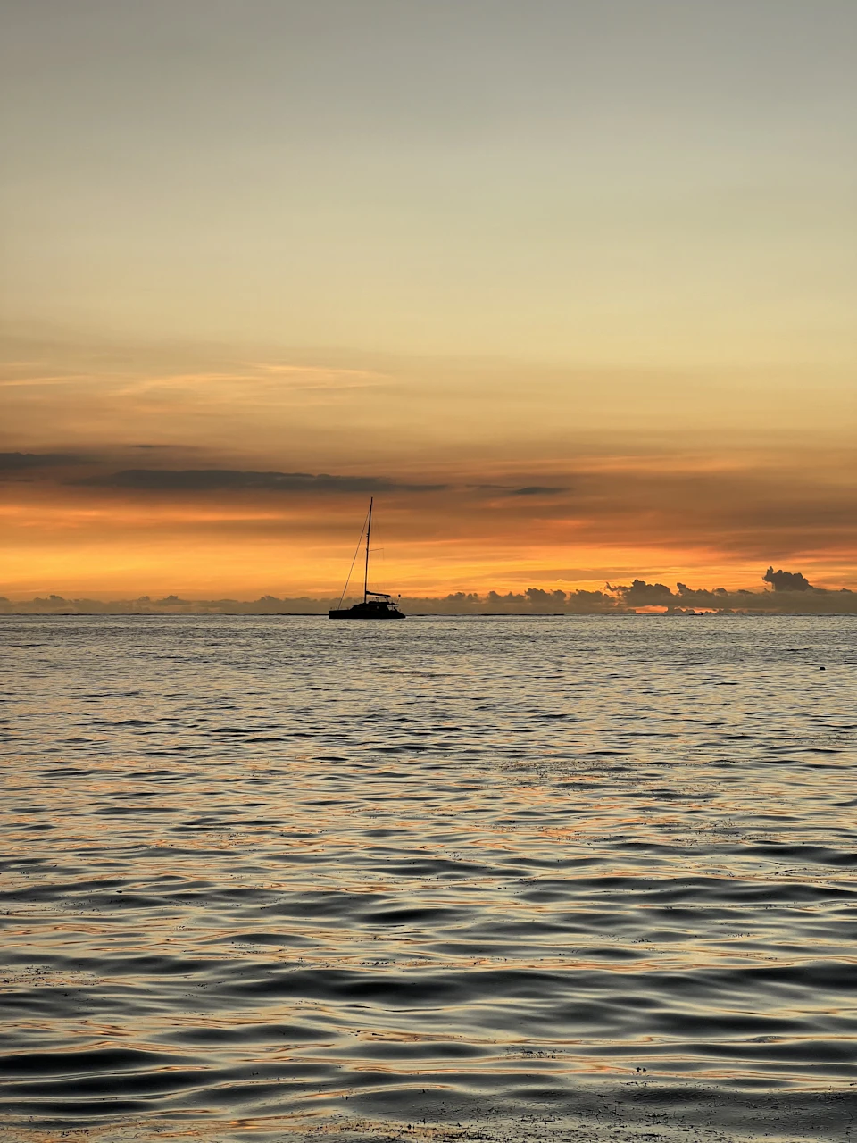 Sailboat sailing into sunset over calm ocean waters with vibrant orange and yellow sky
