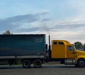 a yellow truck driving down a road next to a forest