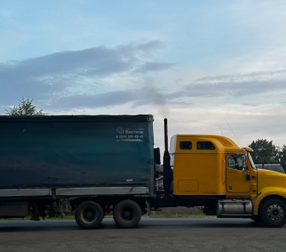 a yellow truck driving down a road next to a forest